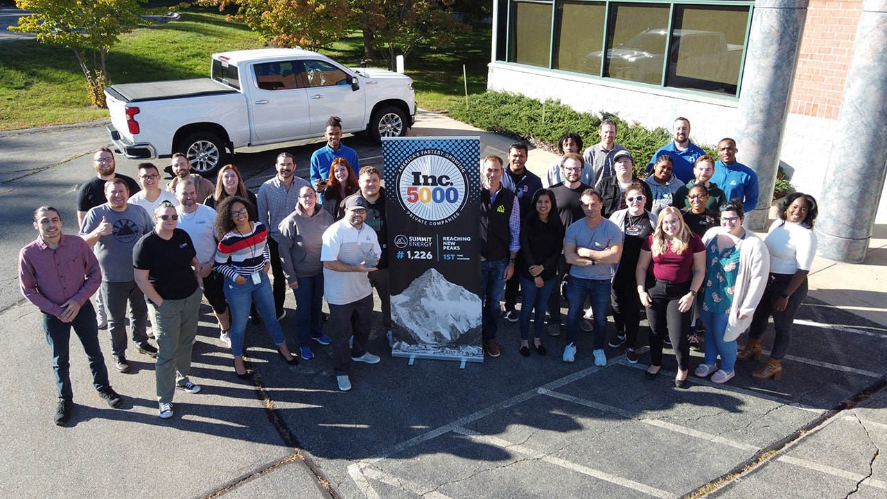 Here is a picture, taken from a drone, that shows a group of MA solar installers. They are standing in a parking lot and they are holding an Inc. 5000 sign given to Summit Energy.