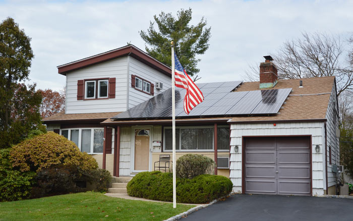 US Flag right next to a Home with Solar Panels installed on its Rooftop